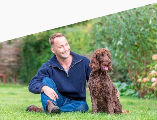 Mies ja hänen koiransa istuvat nurmikolla